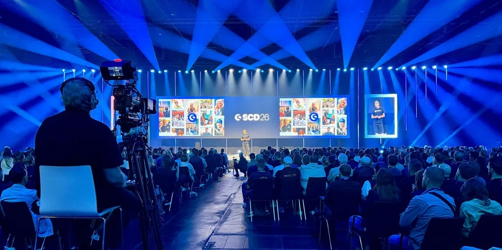 Blick aus dem Publikum auf die blau beleuchtete Hauptbühne des Shopware Community Day 2026 im Confex Köln, im Hintergrund die SCD-26-Leinwand und ein Kamerakran